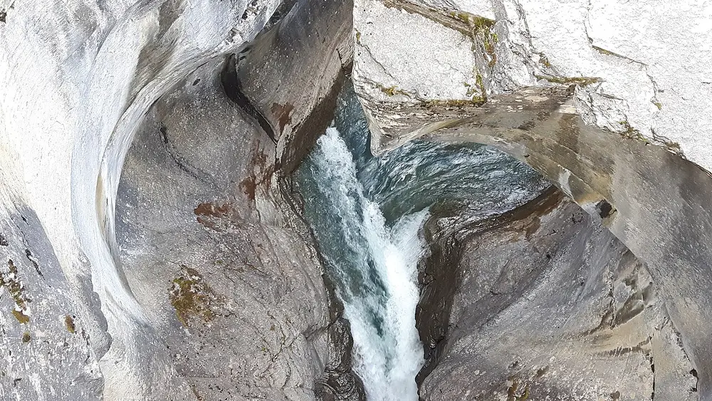 Water forcing through a narrow slot in smooth grey rock at Mistaya Canyon seen from the footbridge above