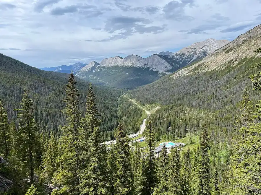 The Miette Hot Springs pools seen from the slope above, small and blue in a forested valley between grey ridges