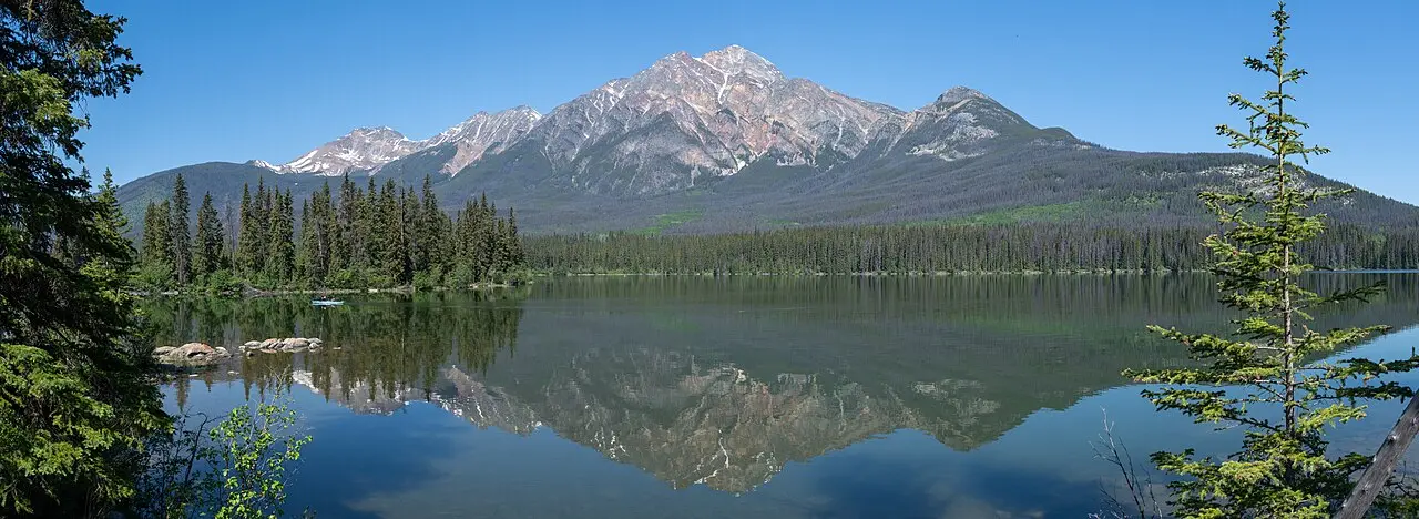 Pyramid Mountain reflected in the still water of Pyramid Lake with spruce forest along both shores