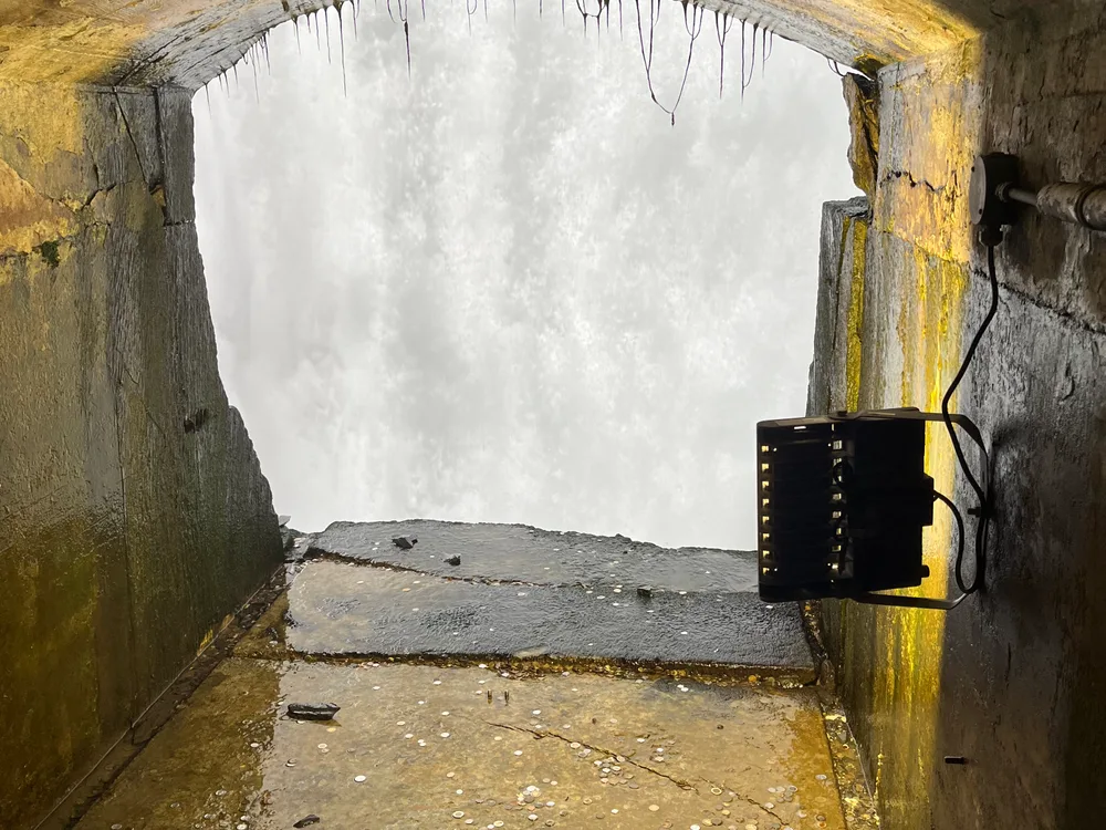 A rock-cut tunnel end opening onto the white water of the falls, with a small floodlight on the wall