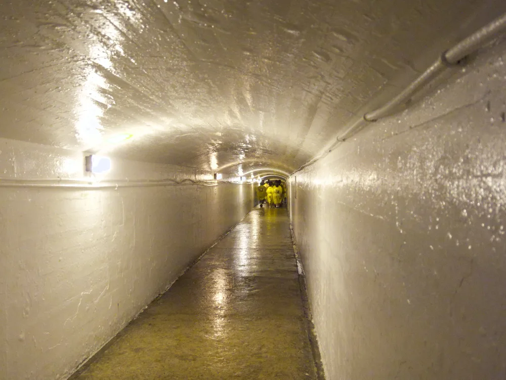 The lit concrete tunnel behind the falls, running away from the camera with visitors in ponchos at the far end
