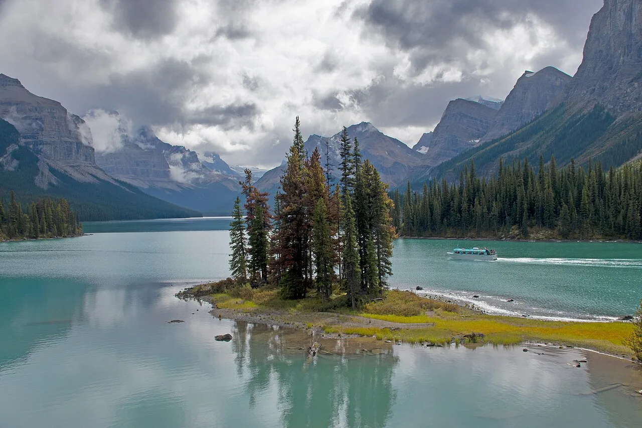 Spirit Island on Maligne Lake with a tour boat passing behind it under a stormy sky
