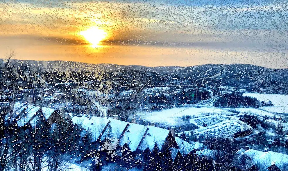 A gondola cabin on a cable above snow-covered Laurentian forest at sunset