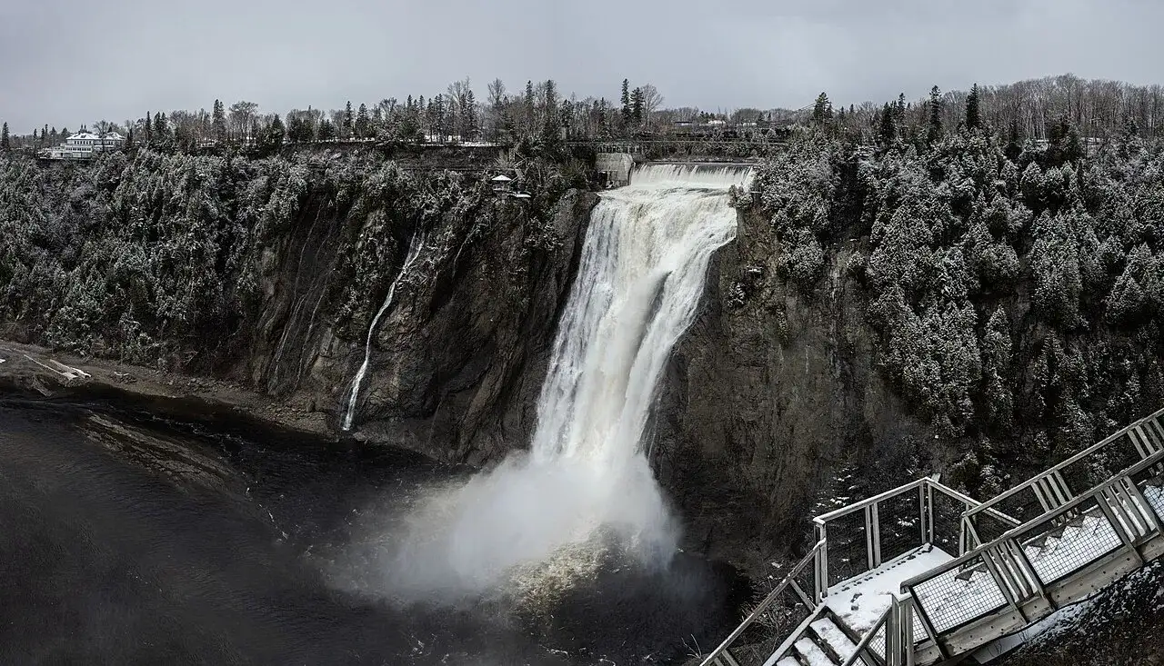Montmorency Falls in winter with the panoramic staircase and Manoir Montmorency visible at the top of the cliff