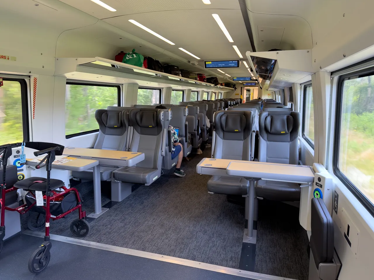 Economy cabin of a VIA Rail Venture car with grey seats, fold-out tables and a wheelchair space by the door