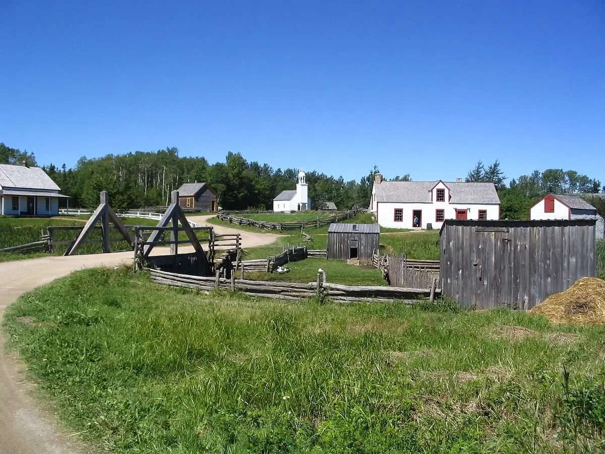 Wooden heritage houses, a white chapel and rail fences on a grassy field at the Village Historique Acadien