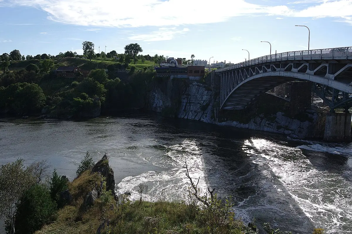 An arched steel bridge crossing a river gorge with churning white rapids below at the Reversing Falls in Saint John