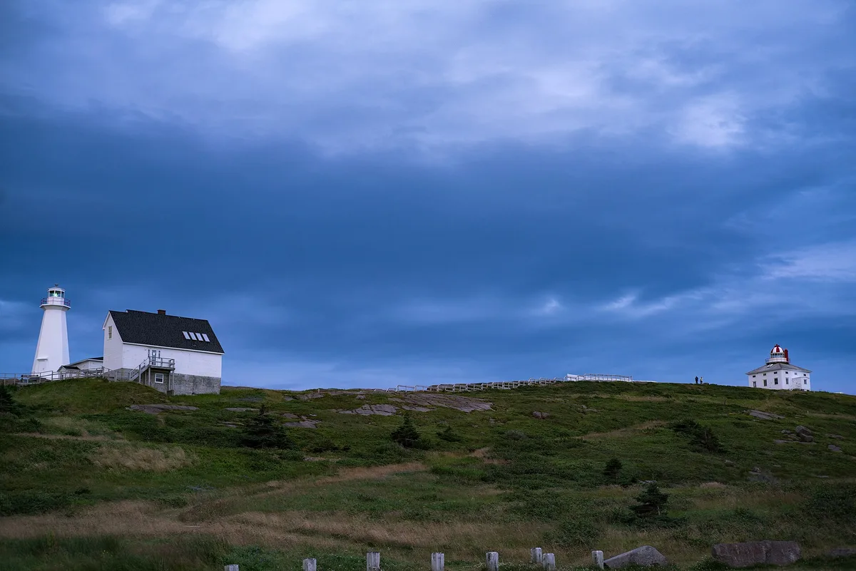 The old and new lighthouses of Cape Spear on a green headland under a heavy blue sky