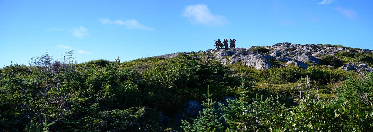 Bronze silhouette sculptures of Norse figures standing on a rocky rise above coastal heath at L'Anse aux Meadows