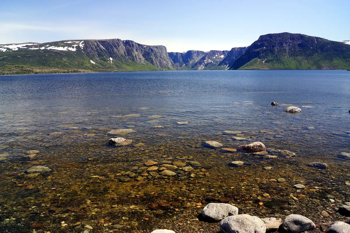 Clear water with rounded boulders in the foreground and steep fjord cliffs rising on both sides at Western Brook Pond