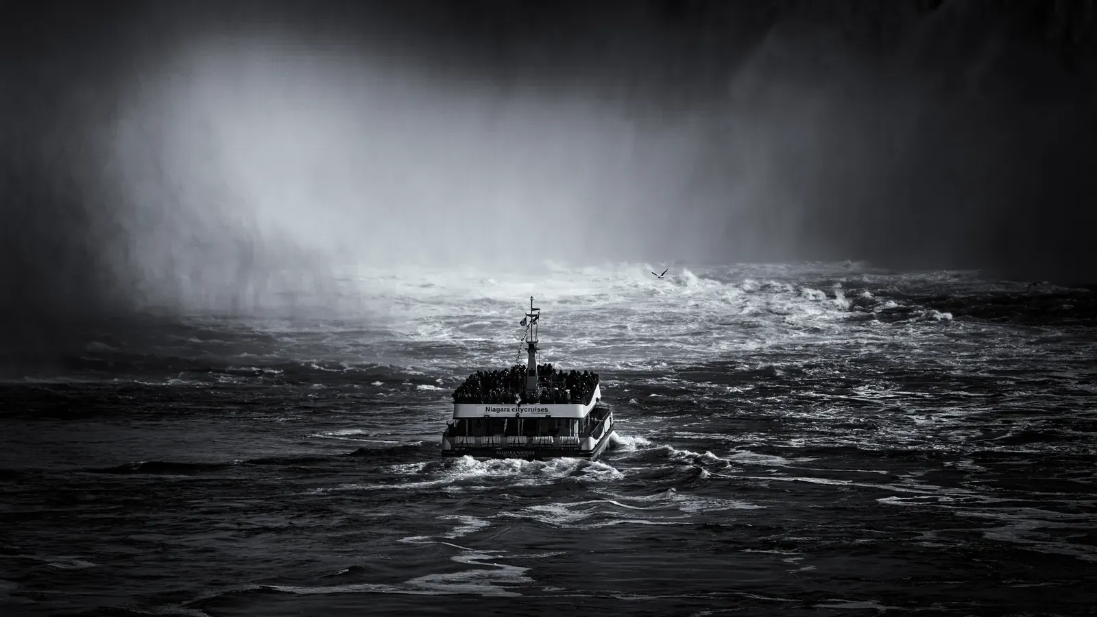 A Niagara City Cruises catamaran heading into the mist wall at the Horseshoe Falls, black-and-white frame