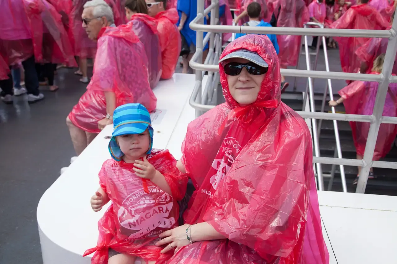 A woman and child in red Hornblower ponchos sitting on a bench on the boat deck in mist