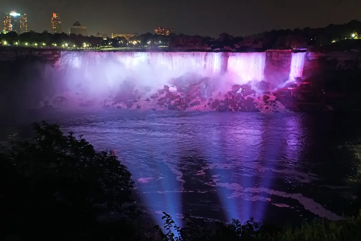 The falls lit in coloured floodlights against the dark sky after nightfall at Niagara