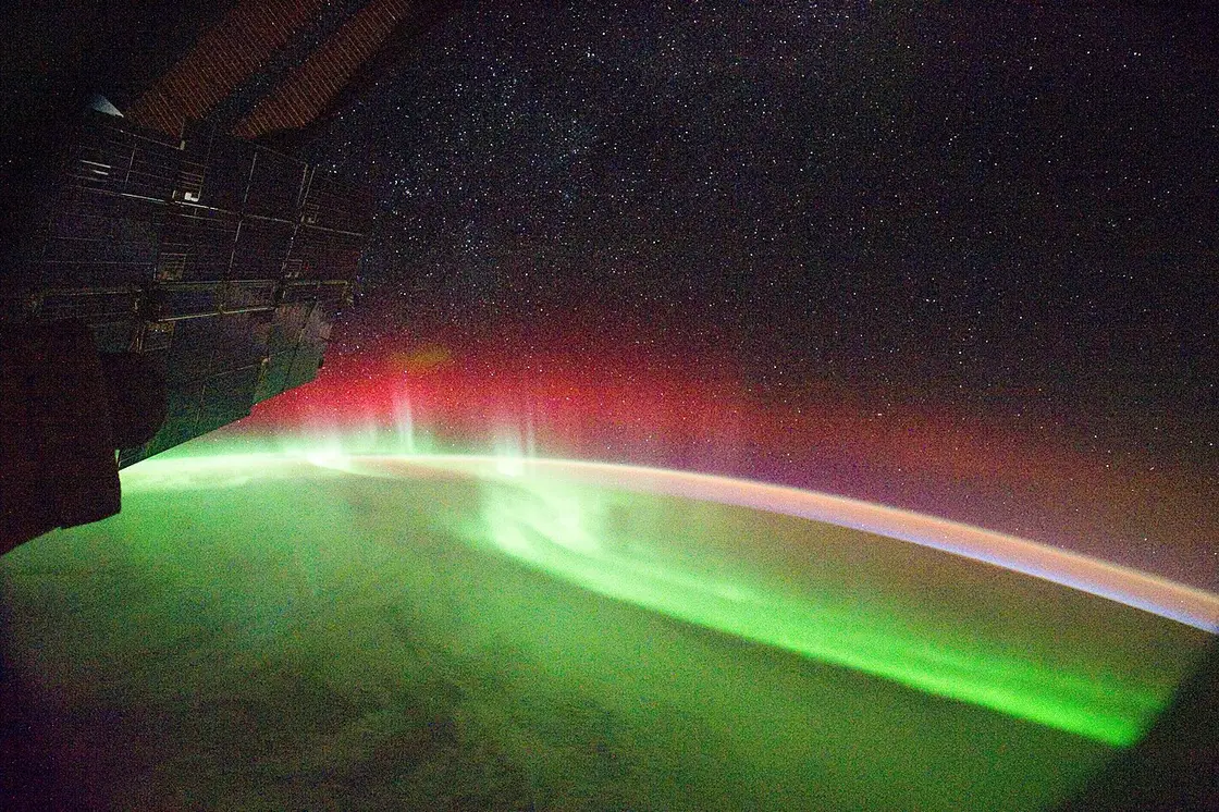 A green and red band of aurora glowing over the curve of the Earth, seen from the International Space Station