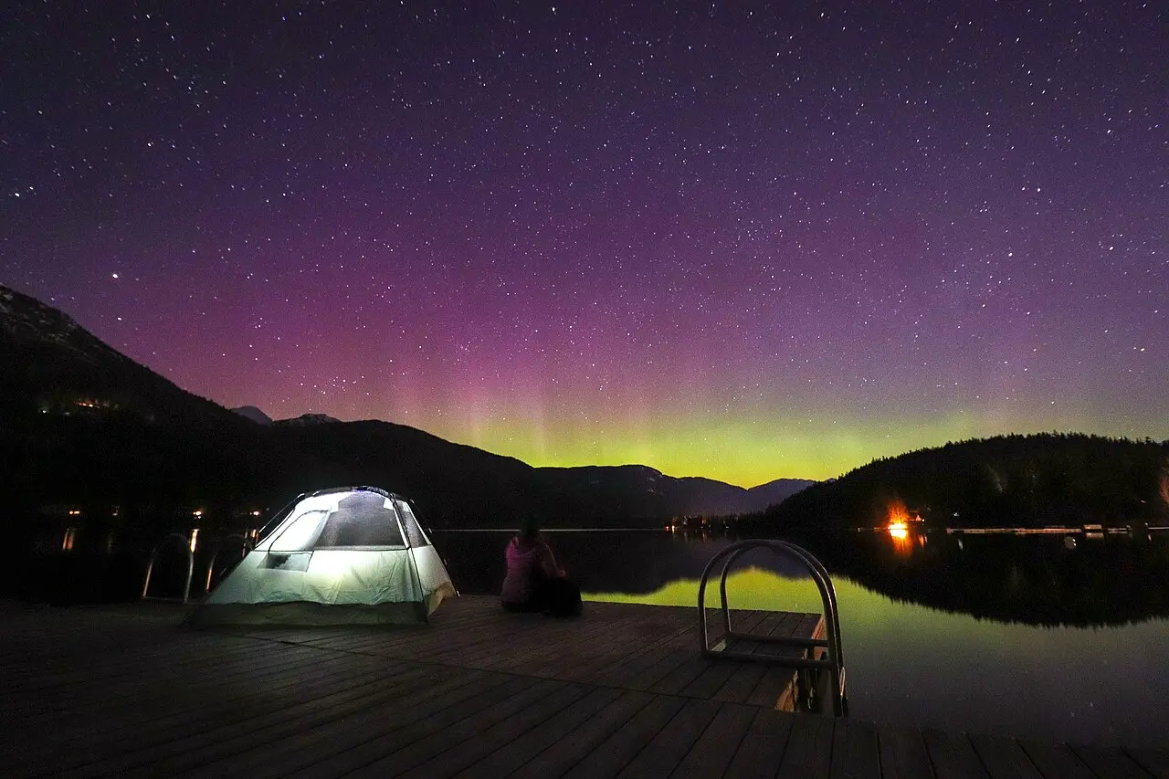A tent lit from within beneath a green aurora beside Great Slave Lake near Yellowknife