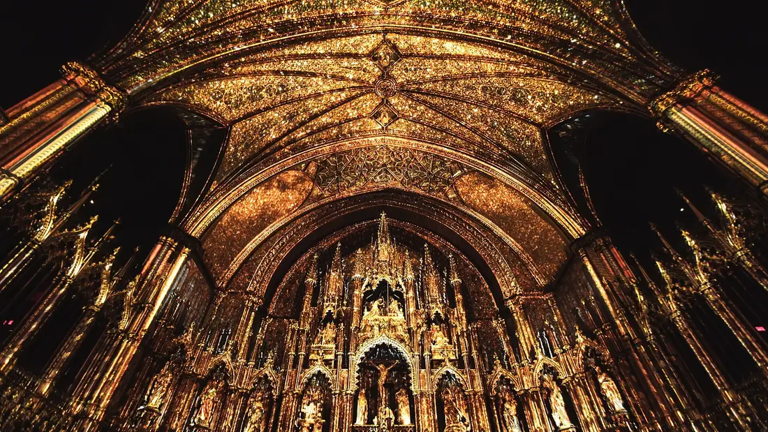 The vault and gilded altarpiece of Notre-Dame Basilica glowing gold under projected light in the dark nave