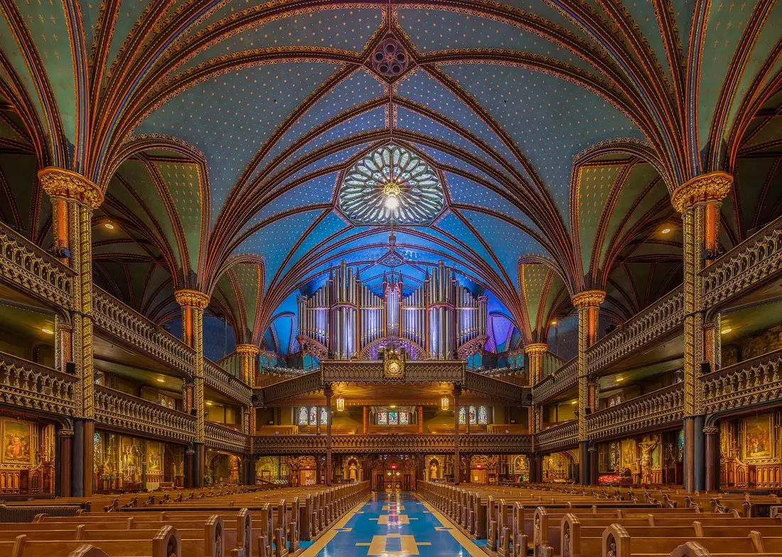 The nave of Notre-Dame Basilica seen from the pews looking back toward the entrance, with the organ pipes in the gallery under the star-studded blue vault