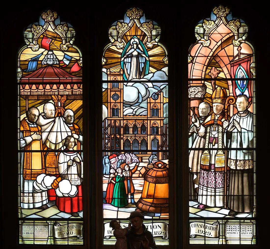 Three stained-glass panels in the nave dated 1910, 1829 and 1929, showing a procession, the church going up and a consecration