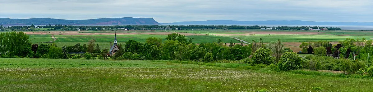 The dyked farmland of Grand-Pré with a memorial church, green fields and the red cliffs of Cape Blomidon in the distance