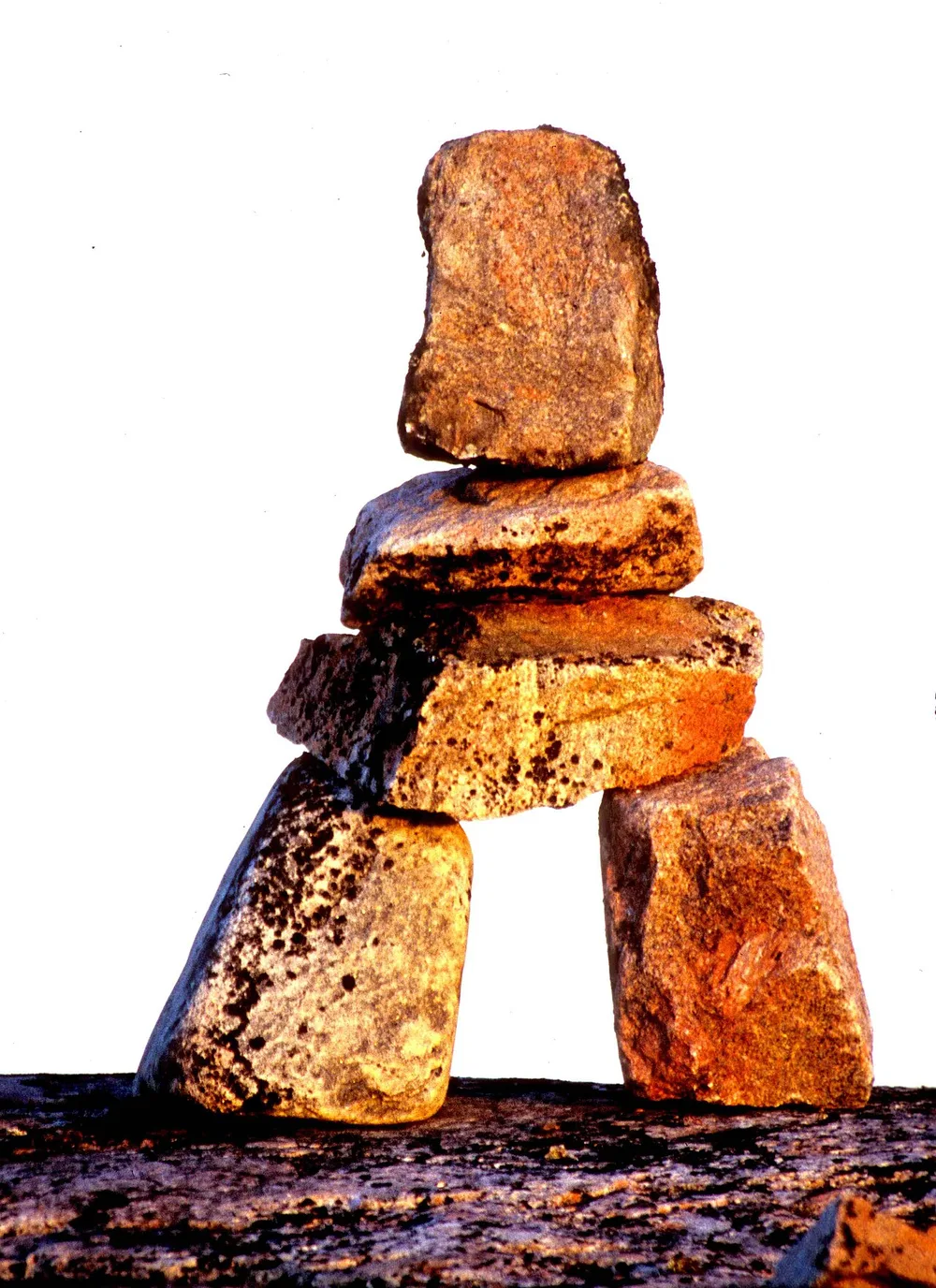 An inuksuk built in a human shape from stacked grey stones standing on the open Arctic tundra