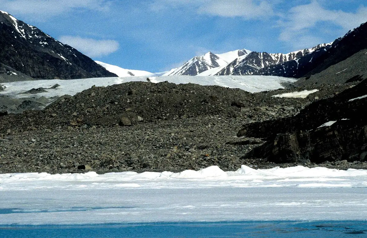 A glacier flowing down to the sea between dark ridges on Bylot Island in Sirmilik National Park