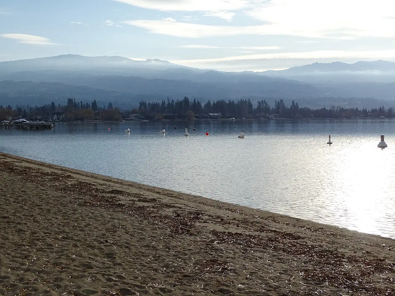 A gravel shoreline on Okanagan Lake near Kelowna with dry hills rising on the far side