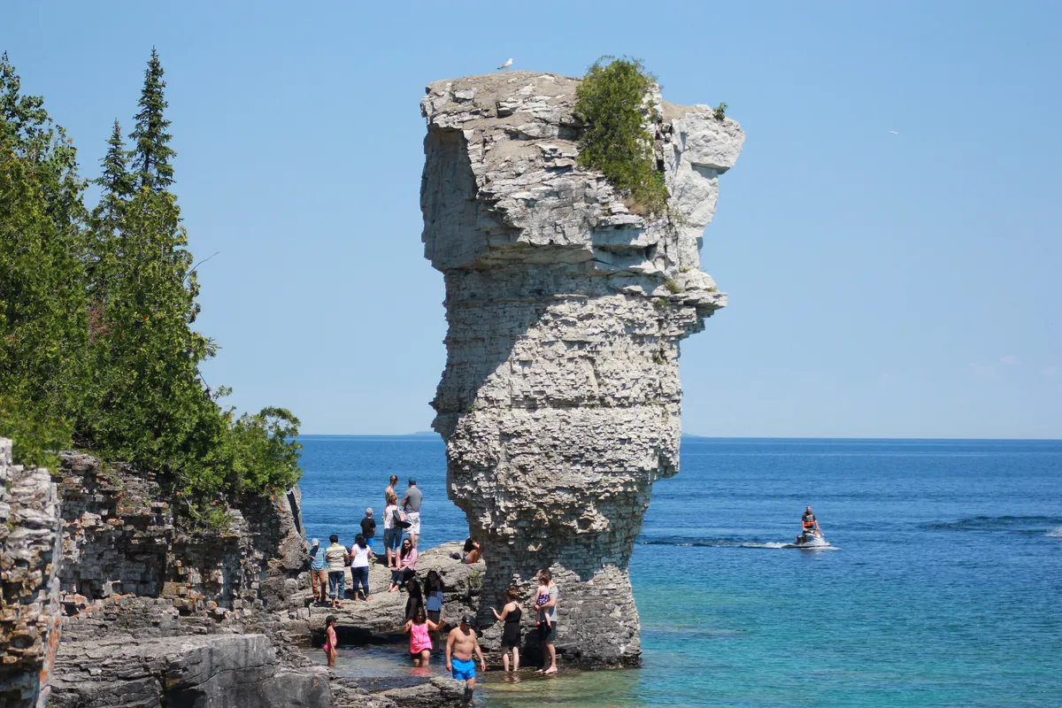 Two tall rock sea stacks rising from the water just off the wooded shore of Flowerpot Island in Lake Huron