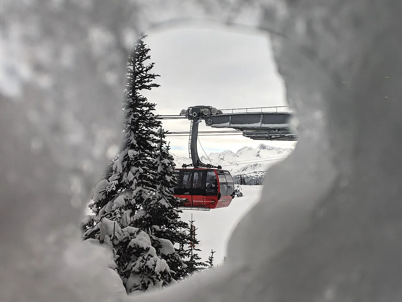 A Peak 2 Peak gondola cabin seen through a gap in snow-covered trees, with mountains in the background