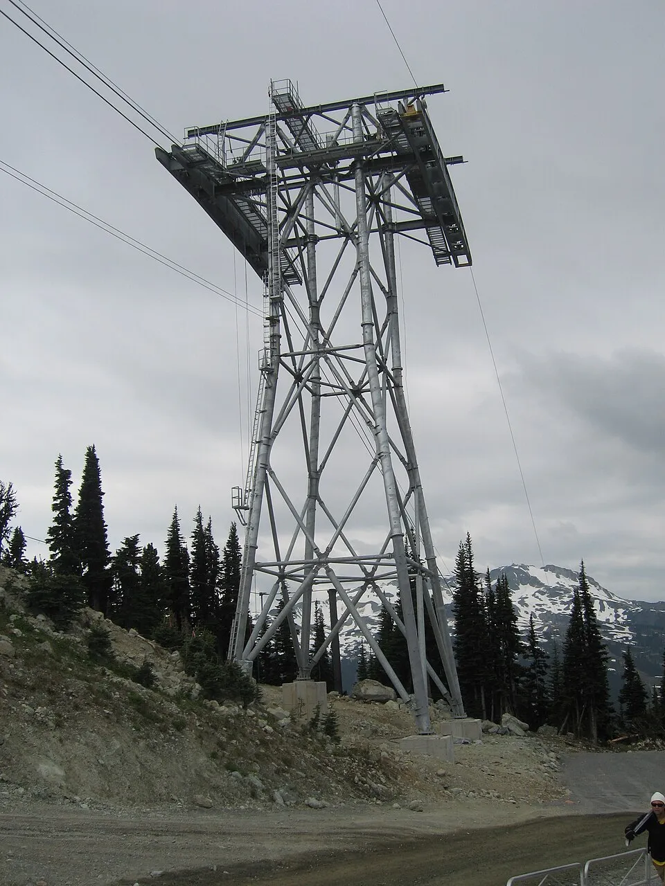 The steel tower structure of the Peak 2 Peak Gondola against a cloudy sky above the treeline