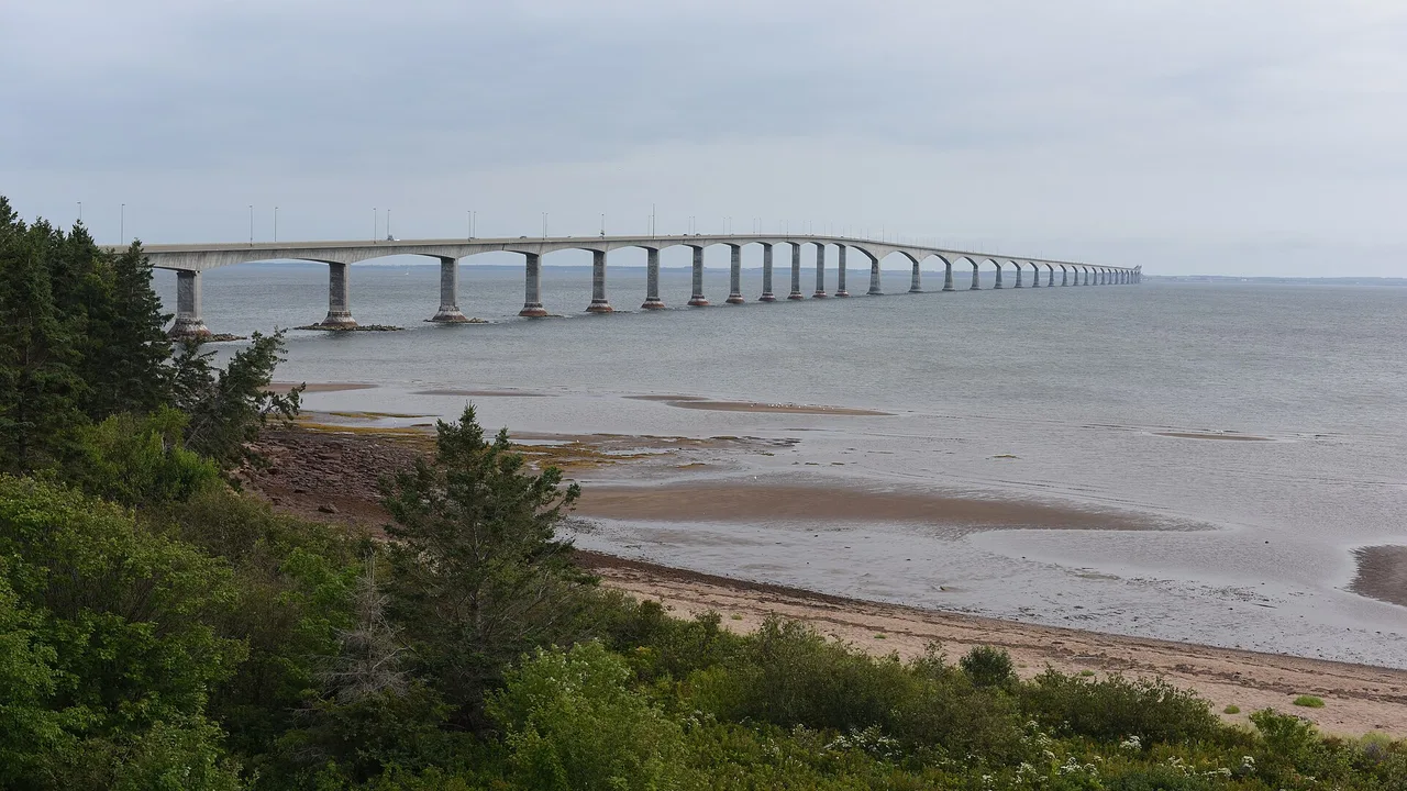 The long multi-span Confederation Bridge stretching across the Northumberland Strait above a red-sand shore