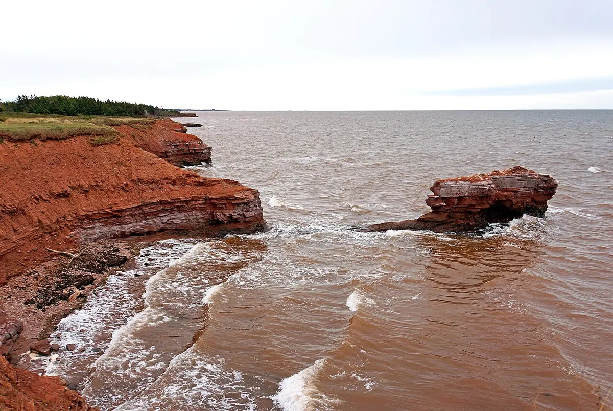 Low red sandstone cliffs and a red-sand shore meeting calm water on the Prince Edward Island coast