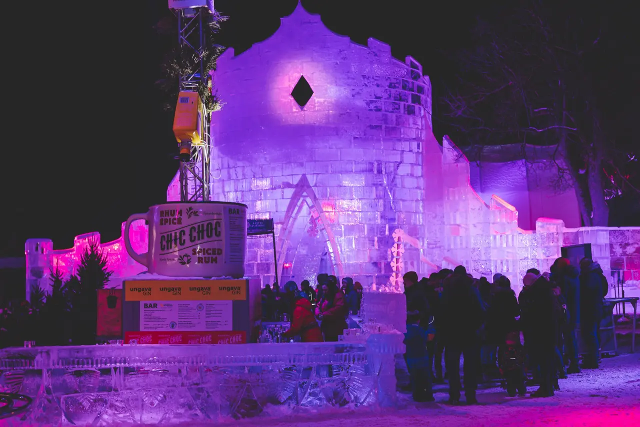 A crowded snowy street at the Quebec Winter Carnival with lights and festival stalls