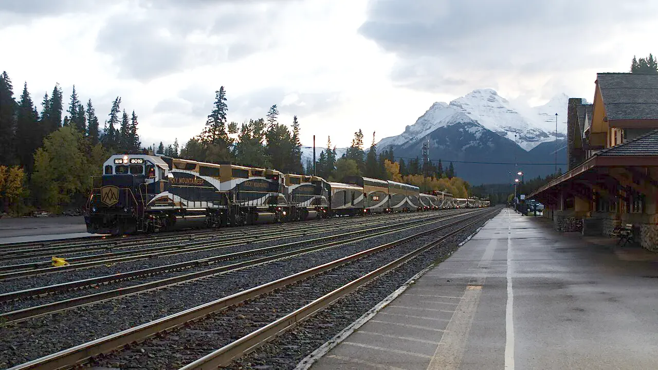 Rocky Mountaineer gold and blue coaches standing at Banff with mountains behind