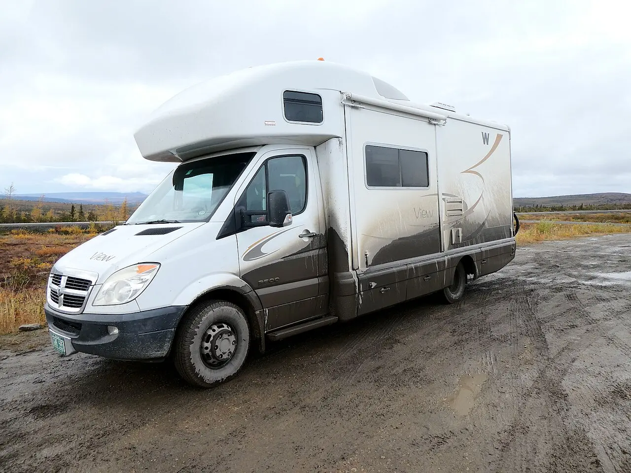 A motorhome parked on the gravel shoulder of the Dempster Highway with bare northern hills behind