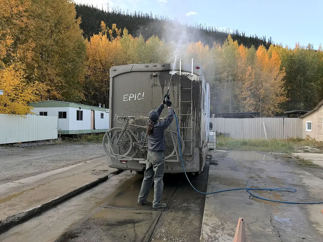 The rear of a motorhome caked in thick grey mud after driving a northern gravel highway