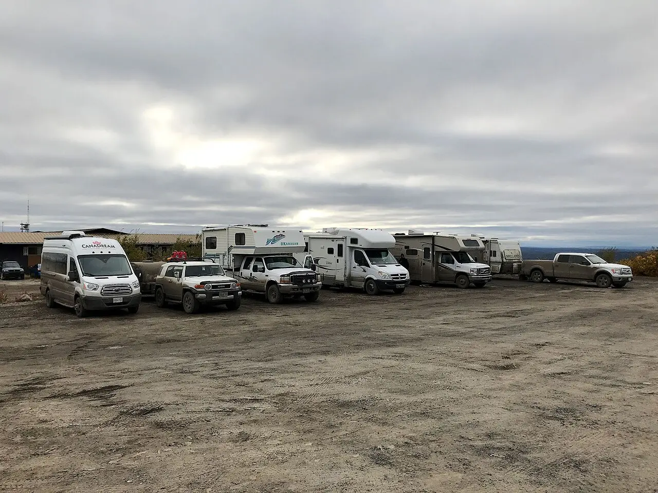 Three motorhomes parked side by side on a gravel lot in northern Canada under a wide grey sky