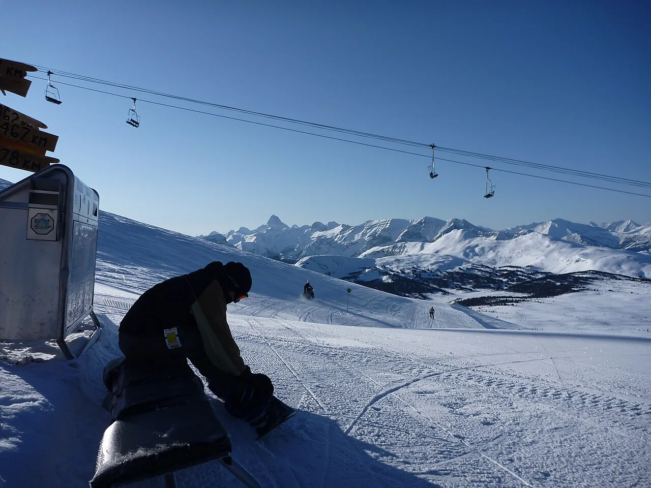 A snowboarder strapping in at the top of a run at Banff Sunshine with Rockies peaks stretching to the horizon
