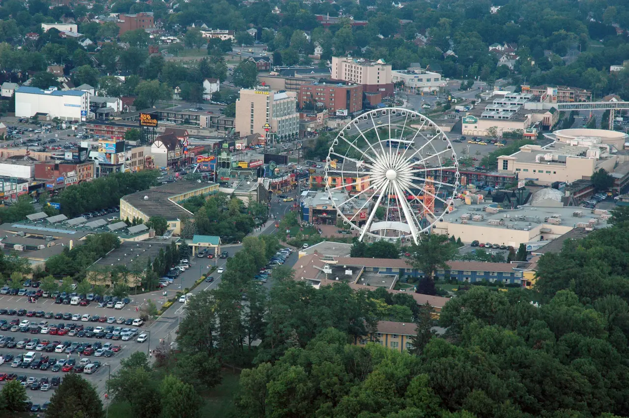 The Niagara SkyWheel and the hotels and attractions of Clifton Hill seen from high above, with parking lots and trees in the foreground