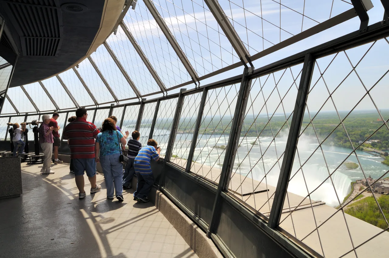 Visitors at the slanted, mesh-covered barrier of the Skylon Tower's observation deck, with the Horseshoe Falls and its mist far below on the right