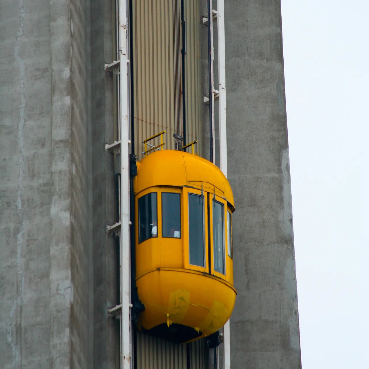 A rounded yellow elevator cabin with tall windows climbing a rail on the concrete shaft of the Skylon Tower