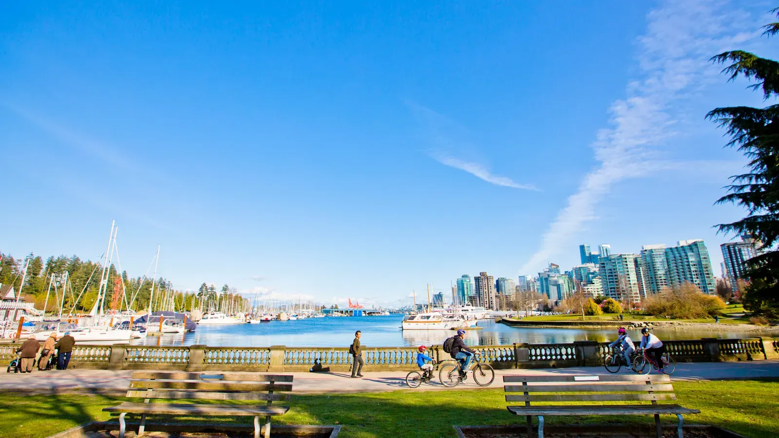 Cyclists and walkers on the Stanley Park Seawall with downtown Vancouver towers across the water