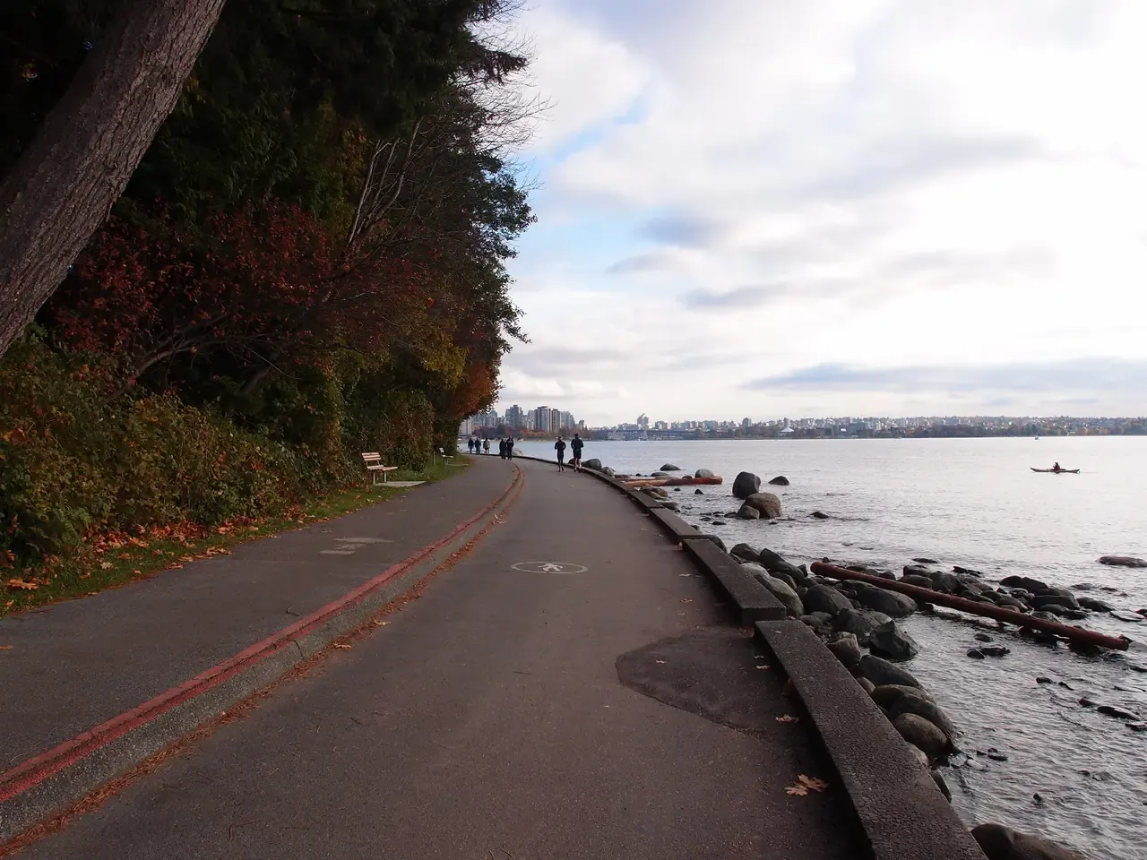 People walking a Stanley Park path with English Bay water and distant mountains beyond