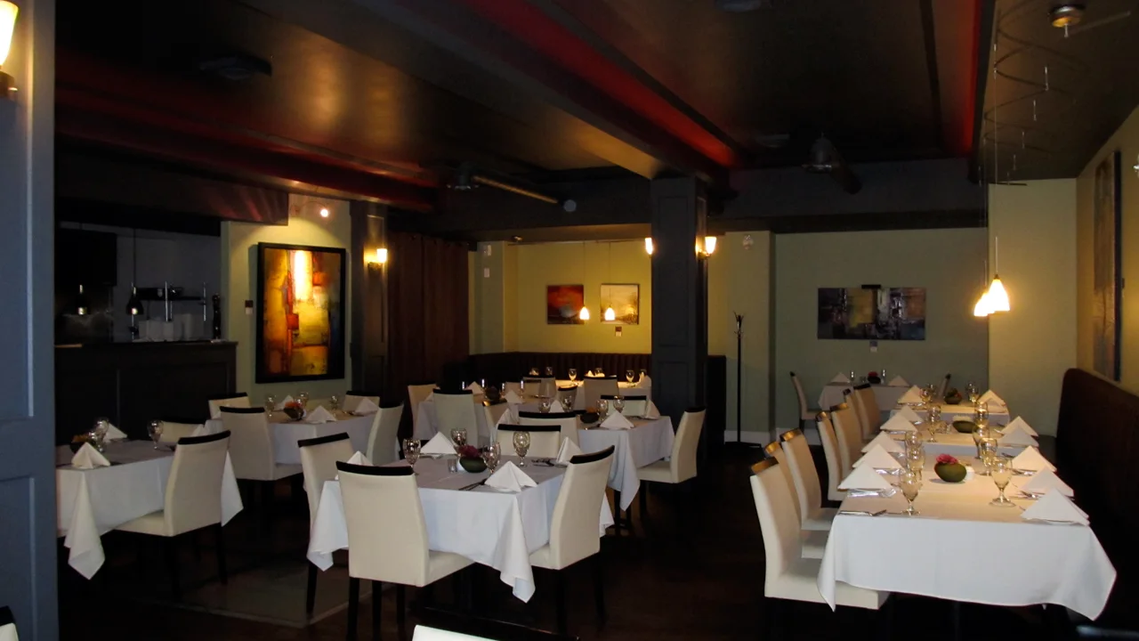 The dining room of a Canadian restaurant set for service, with white tablecloths, wine glasses and low lighting