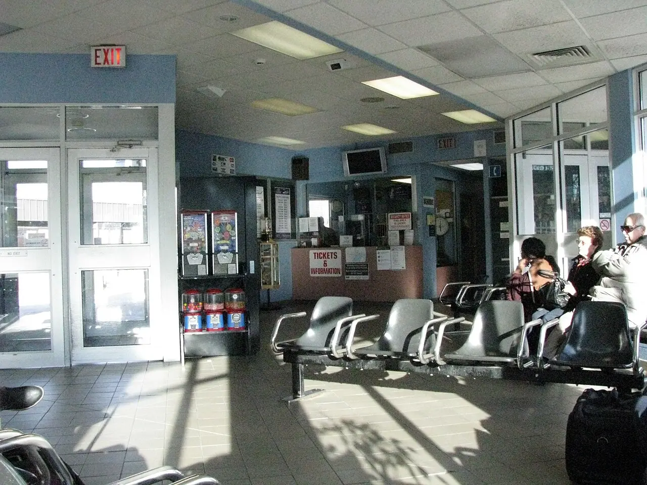 Passengers waiting on benches inside the Niagara Falls transit terminal beside luggage and departure signage