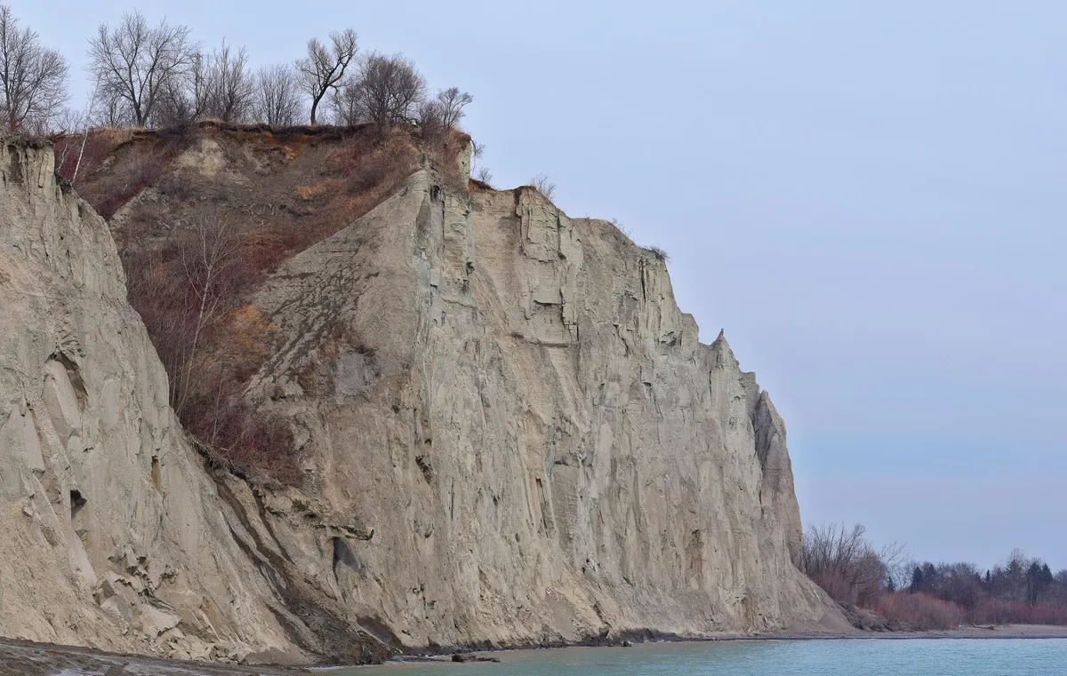 Pale eroded cliffs of the Scarborough Bluffs rising above Lake Ontario and a green park