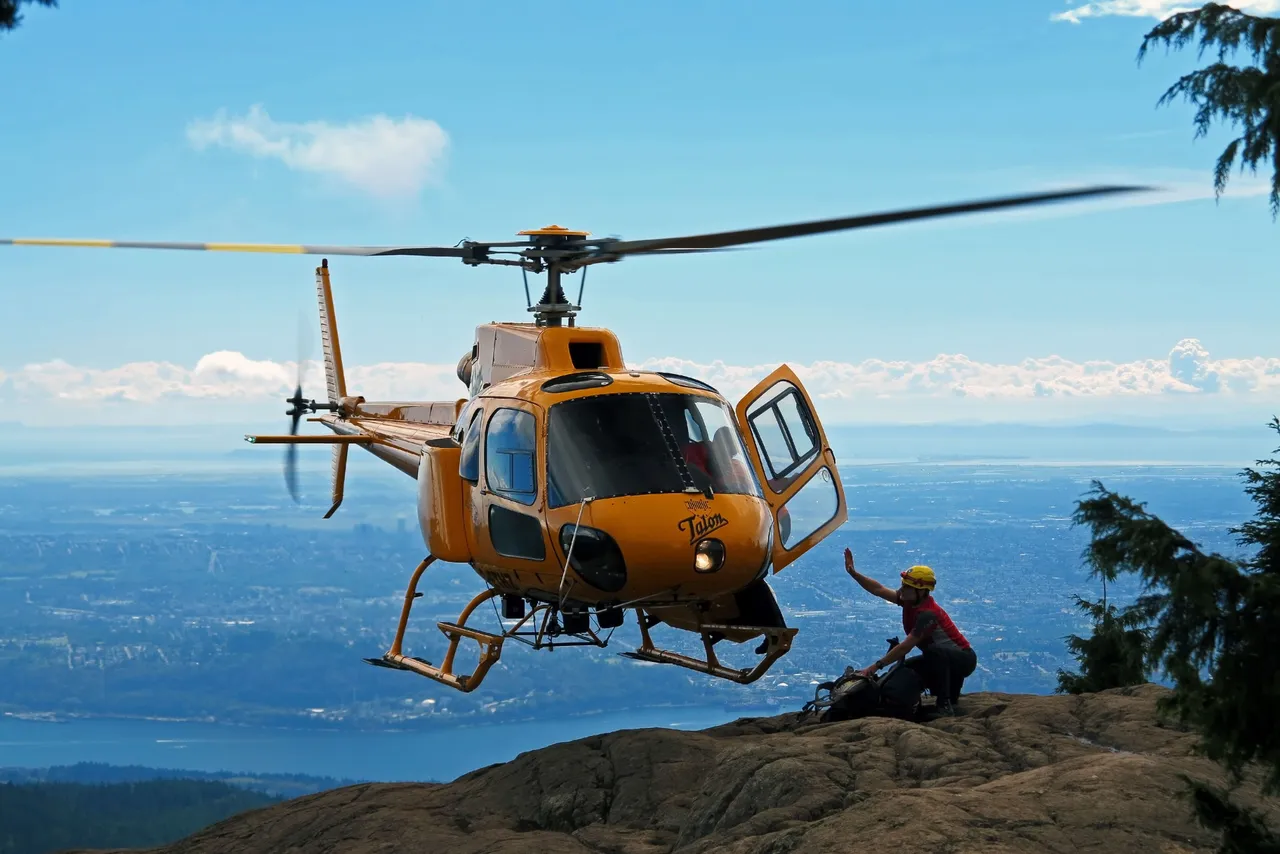 A rescue helicopter hovering over a forested mountain slope during a backcountry rescue in British Columbia