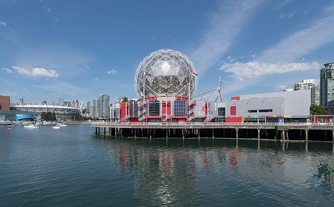 The silver geodesic dome of Science World reflected in the water of False Creek at dusk