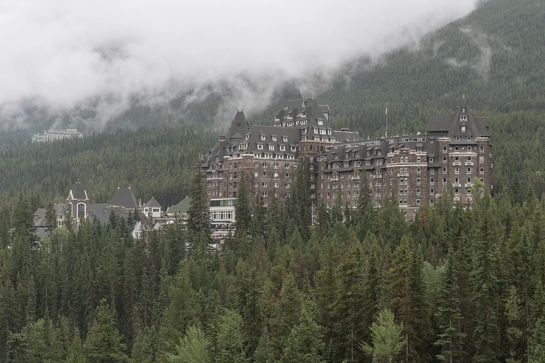 The Fairmont Banff Springs hotel, a stone chateau with green roofs, rising above forested slopes on the Bow River