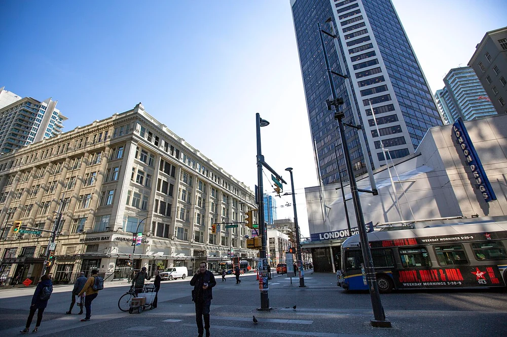 A downtown Vancouver street scene with shops, trees and pedestrians on the pavement