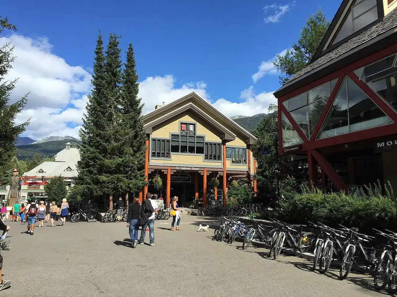The pedestrian core of Whistler Village on a sunny day, with bike rentals, shops and the mountains behind